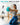 Woman kneeling on a yoga mat and holding a turquoise mini Pilates ball with arms extended forward.