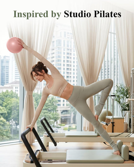 Woman holding a pink mini Pilates ball overhead during a side stretch on a Pilates reformer